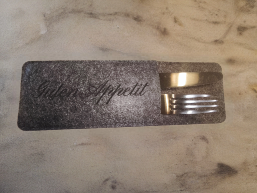 Schwarze Tischmatte mit goldener Schrift und Besteck aus Metall.