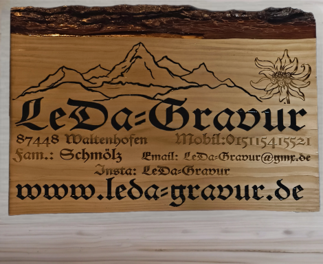 Holzfurnier mit der Gravur „Leda-Gravur“, bergen und Blumenmotiven. Webseite: leda-gravur.de.