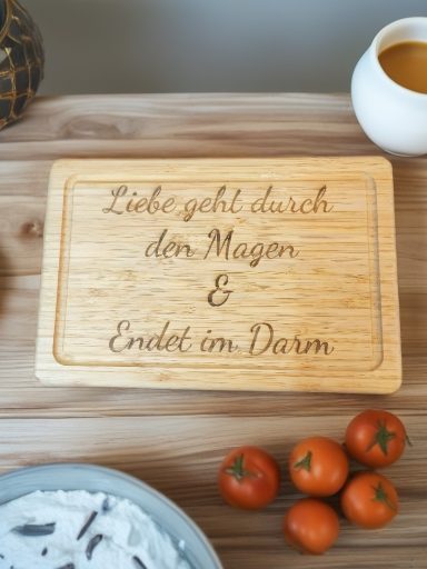 Holzbrett mit der Aufschrift „Liebe geht durch den Magen & endet im Darm“ und kleinen Orangen.
